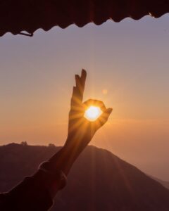 Silhouette of hand forming a circle around the rising sun on a mountain