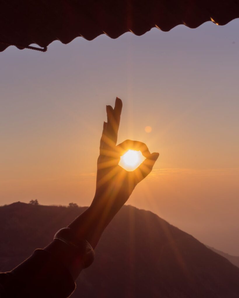 Silhouette of hand forming a circle around the rising sun on a mountain